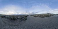 a panoramic view of a street in the middle of nowhere with a cloud filled sky