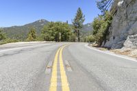 the road is empty and has yellow stripes on the middle one line of it that lead down to a mountain