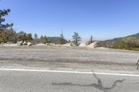 a man on a cell phone standing in the middle of the road with mountains and pine trees in the background