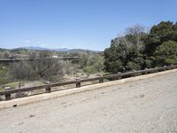 a view from a bridge overlooking trees and a mountain range of hills behind a bridge