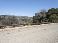 a view from a bridge overlooking trees and a mountain range of hills behind a bridge