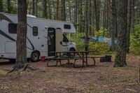 an rv has a table, chairs and a door open in a woods surrounding it