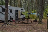 an rv has a table, chairs and a door open in a woods surrounding it