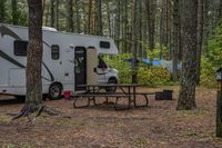 an rv has a table, chairs and a door open in a woods surrounding it