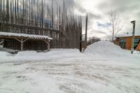 there are piles of snow near the building in front of the snow bank and a wooden structure with bars