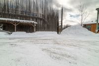 there are piles of snow near the building in front of the snow bank and a wooden structure with bars