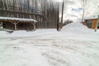 there are piles of snow near the building in front of the snow bank and a wooden structure with bars