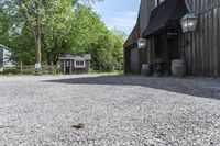 a barn with gravel near by and a horse standing outside it on a farm site