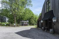 a barn with gravel near by and a horse standing outside it on a farm site