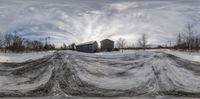 the snow is flowing over the snow field next to a barn under cloudy skies,