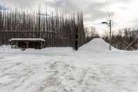 a white snow pile near a wooden fence and a pole in the background and the sky with clouds