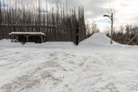 a white snow pile near a wooden fence and a pole in the background and the sky with clouds