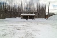 a snow covered sidewalk next to a covered building and a snowy hill and trees behind