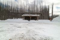 a snow covered sidewalk next to a covered building and a snowy hill and trees behind