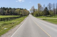 a country highway runs along the side of the road surrounded by fenced in field and woods