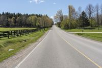 a country highway runs along the side of the road surrounded by fenced in field and woods