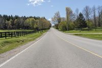 a country highway runs along the side of the road surrounded by fenced in field and woods