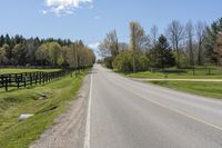 a country highway runs along the side of the road surrounded by fenced in field and woods