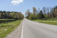 a country highway runs along the side of the road surrounded by fenced in field and woods