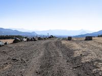 a dirt road in the middle of some rocks and a mountain range in the distance