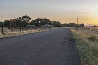 a long empty road in the country with some trees around it, and a fence to the side of the road