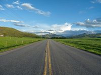 a lone country road is in the countryside area with mountains on both sides and barbed fence between the two sides