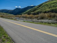 the road is paved with yellow markings and has a snowy mountain range in the background