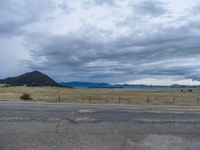 a long street passes a prairie area and mountains in the distance with heavy clouds in the sky