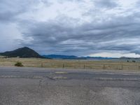 a long street passes a prairie area and mountains in the distance with heavy clouds in the sky