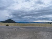 a long street passes a prairie area and mountains in the distance with heavy clouds in the sky