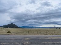 a long street passes a prairie area and mountains in the distance with heavy clouds in the sky