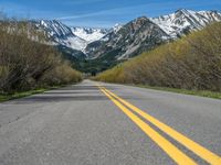 the road is paved with yellow markings and has a snowy mountain range in the background