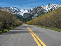 the road is paved with yellow markings and has a snowy mountain range in the background