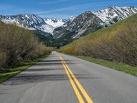 the road is paved with yellow markings and has a snowy mountain range in the background