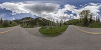 two lanes and a cloudy sky in front of some trees and mountains, with a mountain range in the background