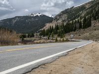 a mountain side with a road running next to the mountains, a bike parked in front of it and trees on one side