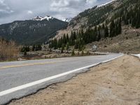 a mountain side with a road running next to the mountains, a bike parked in front of it and trees on one side