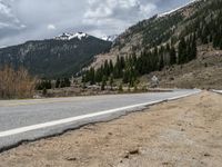 a mountain side with a road running next to the mountains, a bike parked in front of it and trees on one side