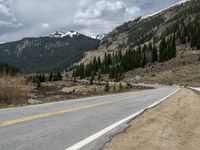 a mountain side with a road running next to the mountains, a bike parked in front of it and trees on one side