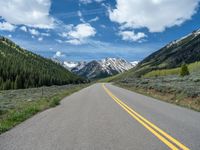 the road is paved with yellow markings and has a snowy mountain range in the background