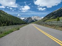 the road is paved with yellow markings and has a snowy mountain range in the background