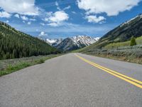 the road is paved with yellow markings and has a snowy mountain range in the background