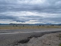 a long street passes a prairie area and mountains in the distance with heavy clouds in the sky