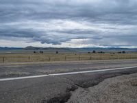 a long street passes a prairie area and mountains in the distance with heavy clouds in the sky