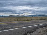 a long street passes a prairie area and mountains in the distance with heavy clouds in the sky