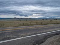 a long street passes a prairie area and mountains in the distance with heavy clouds in the sky