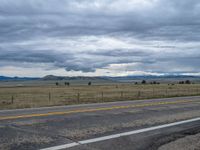 a long street passes a prairie area and mountains in the distance with heavy clouds in the sky