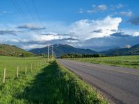 a lone country road is in the countryside area with mountains on both sides and barbed fence between the two sides