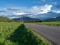 a lone country road is in the countryside area with mountains on both sides and barbed fence between the two sides