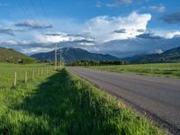 a lone country road is in the countryside area with mountains on both sides and barbed fence between the two sides